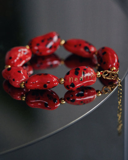 Купіть виріб ручної роботи Red Speckled "Beans" Bracelet від Nadiia World. Ідеальний вибір для додавання вишуканості та шарму до вашого житлового простору або колекції особистих аксесуарів.
